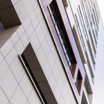Ground view of tall building facade, fenced with beige square tiles.